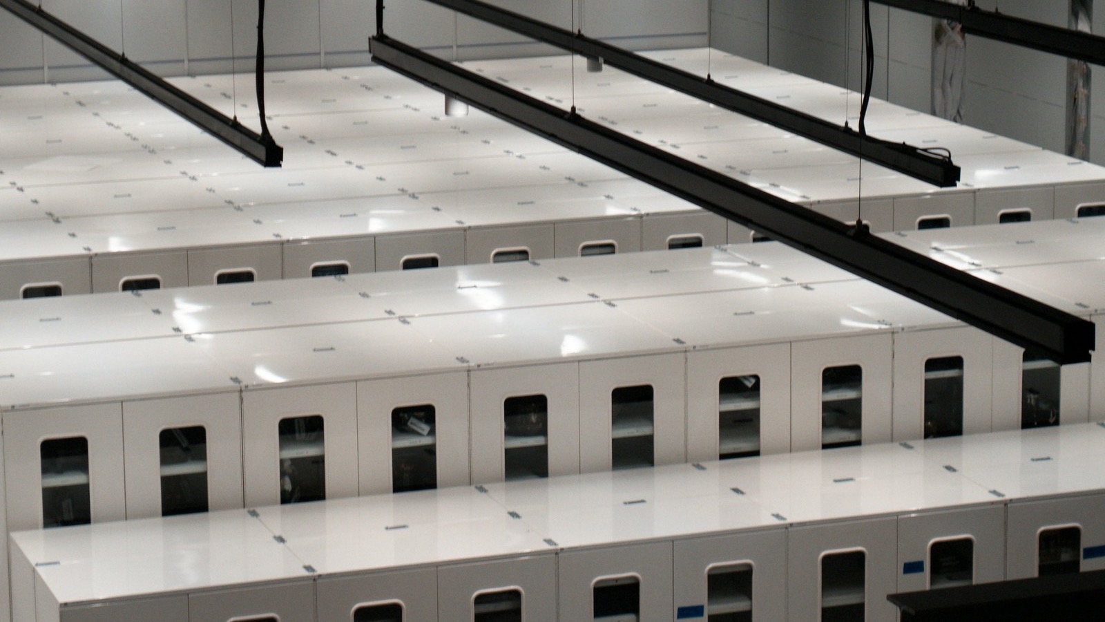 Rows of white server cabinets under hanging cable trays in a data centre.