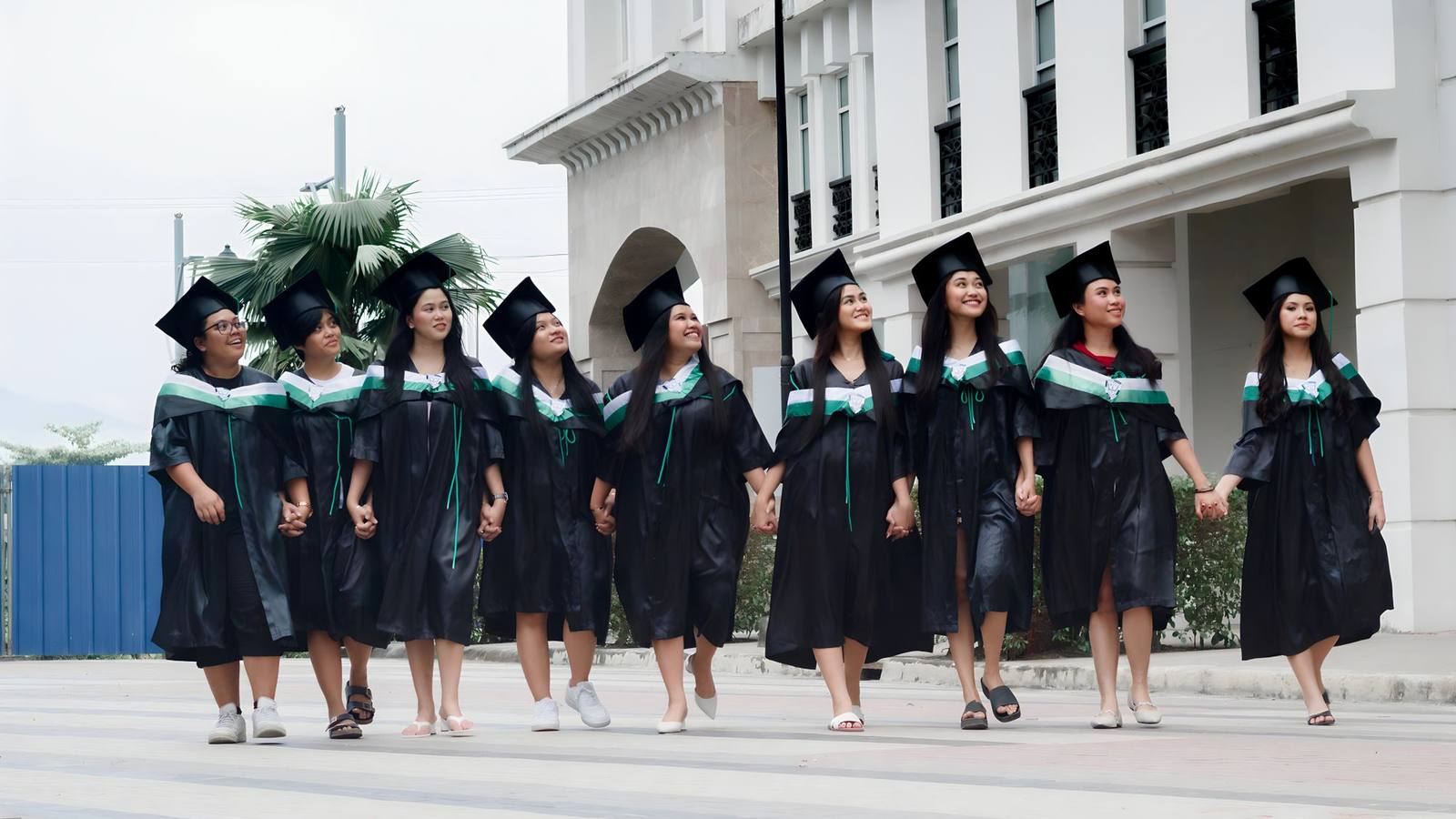 Smiling graduates in caps and gowns walking together outdoors on a sunny day.