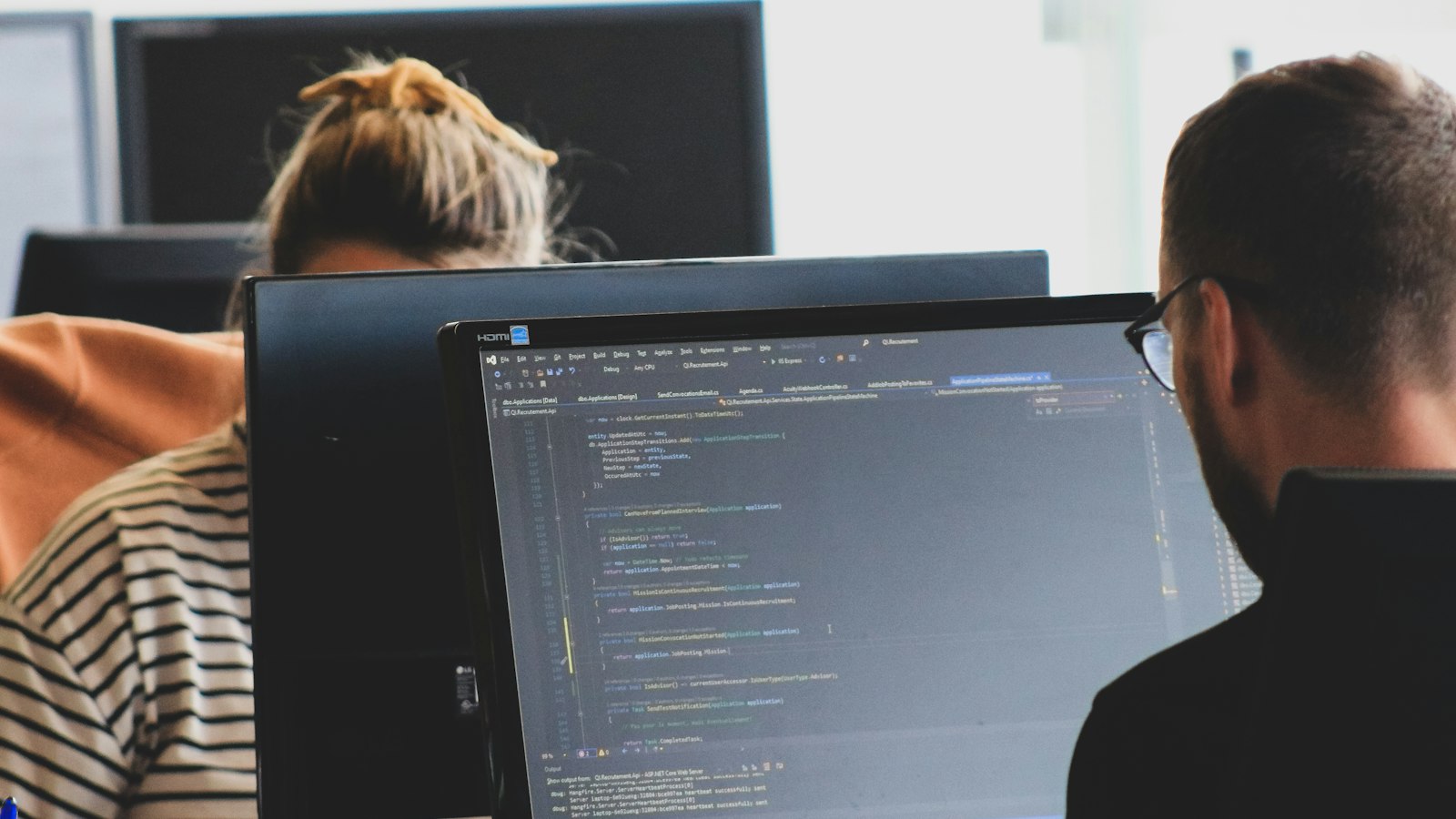 Two colleagues reviewing code on monitors in a bright office