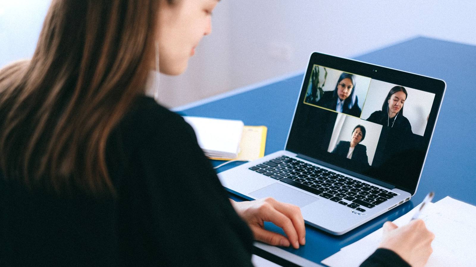 A woman on a video call on her laptop at home, taking notes.
